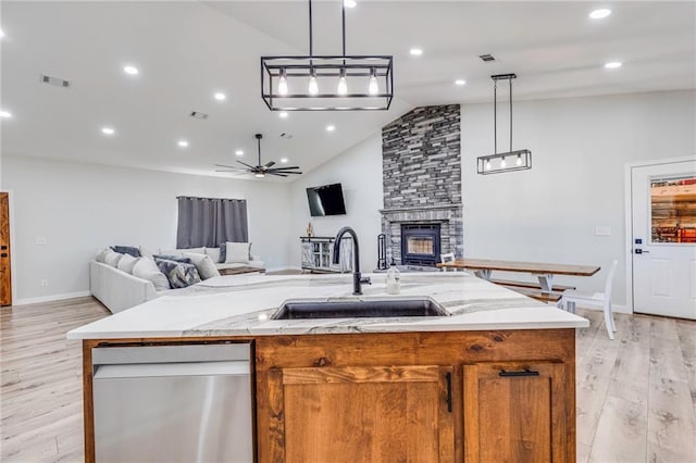 kitchen with sink, decorative light fixtures, a fireplace, and an island with sink