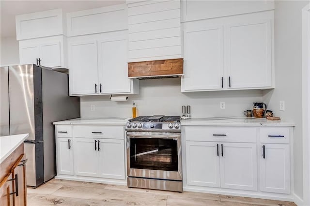 kitchen with white cabinetry, custom exhaust hood, light hardwood / wood-style floors, and appliances with stainless steel finishes