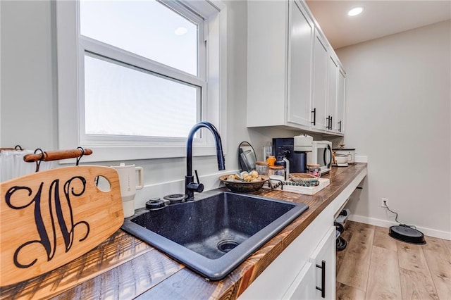 kitchen featuring white cabinetry, sink, wood counters, and light hardwood / wood-style floors