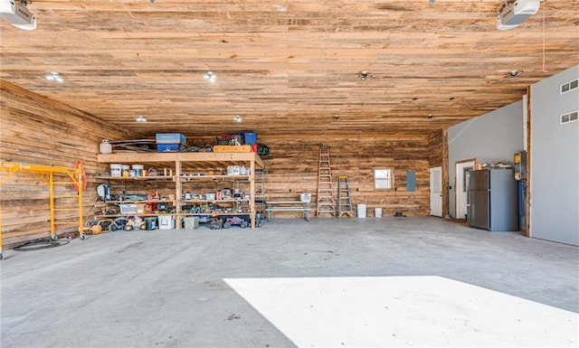 garage featuring wood ceiling, stainless steel fridge, and a workshop area