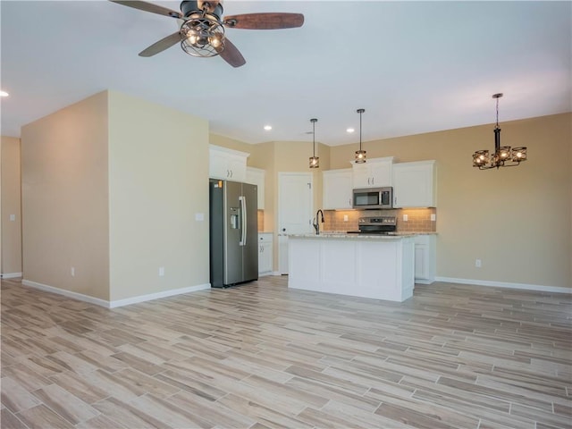 kitchen featuring decorative light fixtures, a center island with sink, white cabinets, stainless steel appliances, and backsplash