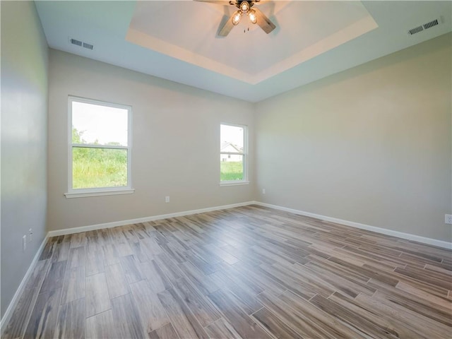 empty room featuring a tray ceiling, light hardwood / wood-style flooring, and ceiling fan