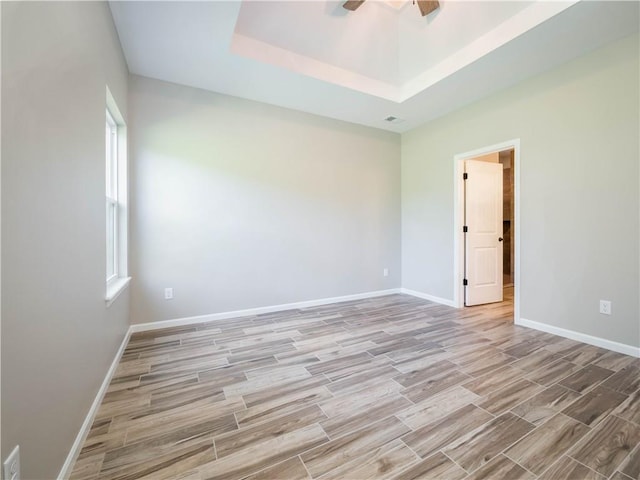 empty room with ceiling fan and a raised ceiling