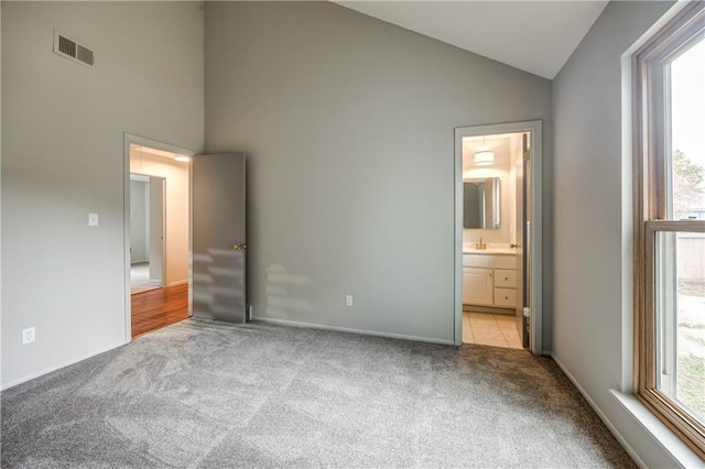 unfurnished bedroom with light carpet, high vaulted ceiling, and ensuite bathroom