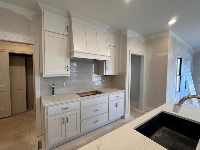 kitchen with backsplash, white cabinets, sink, and black cooktop