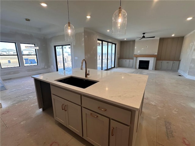 kitchen with pendant lighting, an island with sink, sink, and light stone counters