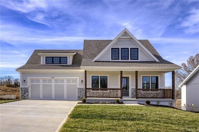 view of front of house featuring covered porch, an attached garage, a front yard, stone siding, and driveway