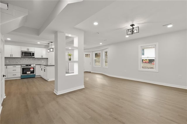 kitchen with tasteful backsplash, hanging light fixtures, light wood-type flooring, appliances with stainless steel finishes, and white cabinets