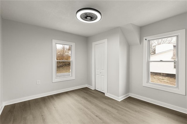 unfurnished bedroom featuring a closet, multiple windows, baseboards, and wood finished floors