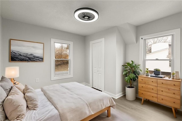 bedroom with a textured ceiling, multiple windows, light wood-type flooring, and baseboards