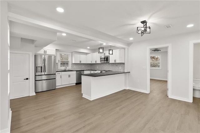 kitchen featuring stainless steel appliances, a peninsula, a sink, tasteful backsplash, and dark countertops