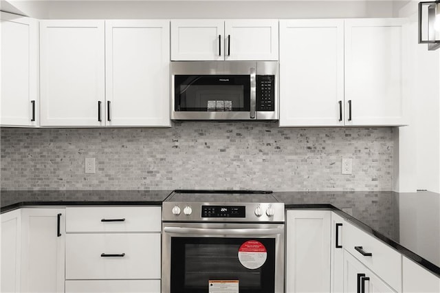 kitchen with stainless steel appliances, white cabinets, dark stone countertops, and tasteful backsplash