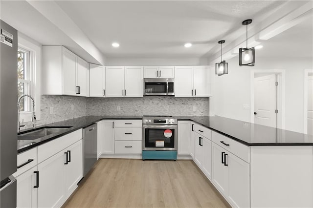 kitchen with light wood finished floors, stainless steel appliances, white cabinets, a sink, and a peninsula