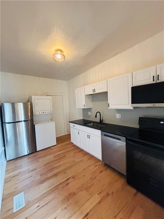 kitchen with sink, white cabinetry, stainless steel appliances, stacked washer / drying machine, and light hardwood / wood-style floors