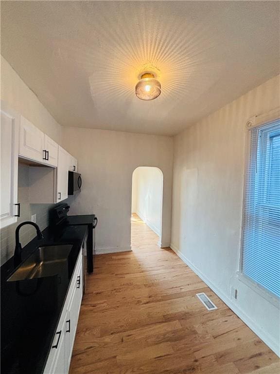 kitchen with sink, black appliances, white cabinets, and light wood-type flooring