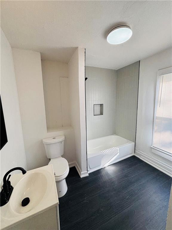 full bathroom featuring hardwood / wood-style floors, tiled shower / bath combo, vanity, a textured ceiling, and toilet