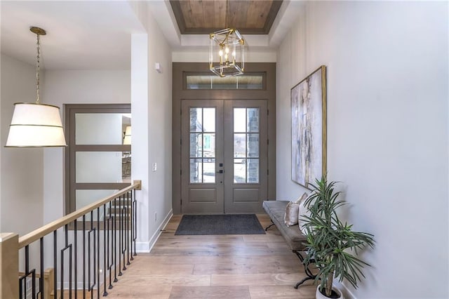 foyer entrance with hardwood / wood-style floors, a notable chandelier, french doors, and a raised ceiling