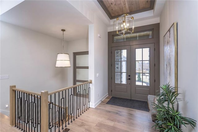 entryway featuring an inviting chandelier, light hardwood / wood-style flooring, a raised ceiling, and french doors