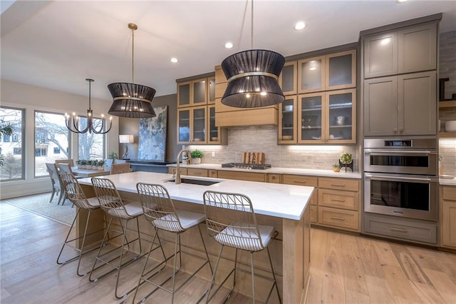 kitchen featuring sink, appliances with stainless steel finishes, hanging light fixtures, tasteful backsplash, and a center island with sink