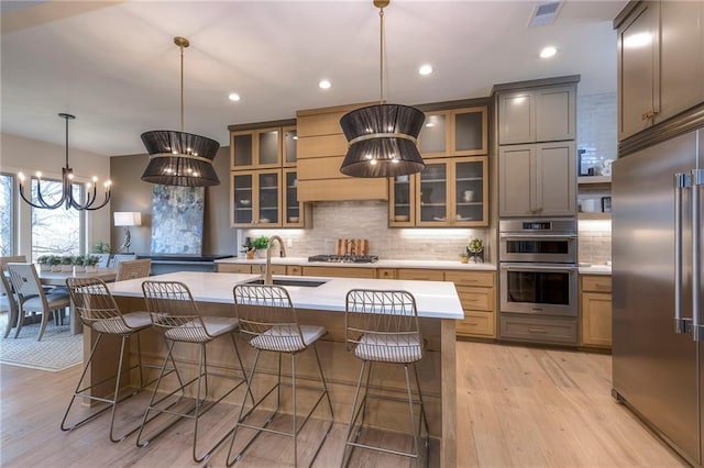 kitchen with a breakfast bar, decorative light fixtures, an island with sink, sink, and stainless steel appliances