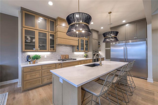 kitchen with a kitchen island with sink, hanging light fixtures, sink, and appliances with stainless steel finishes