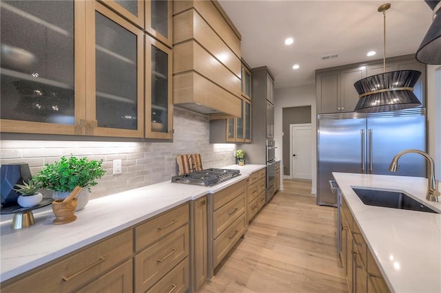 kitchen with sink, hanging light fixtures, stainless steel appliances, light stone countertops, and light hardwood / wood-style flooring