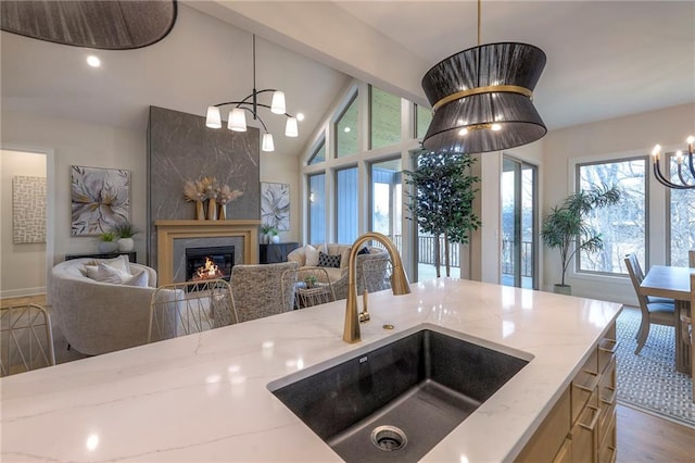 kitchen with sink, an inviting chandelier, hanging light fixtures, vaulted ceiling with beams, and light stone countertops