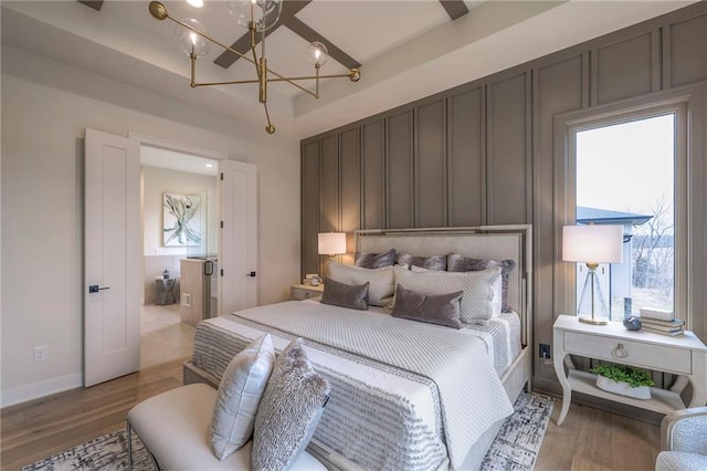 bedroom with a notable chandelier, light hardwood / wood-style floors, and a raised ceiling