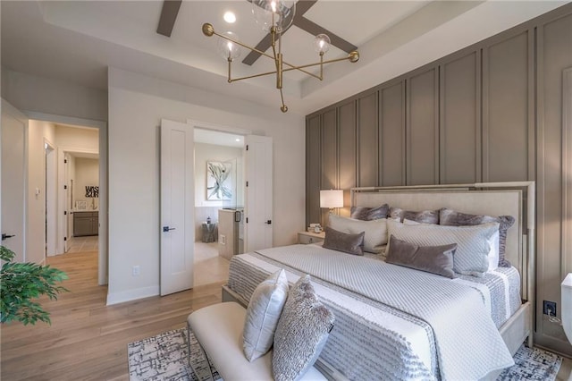 bedroom featuring an inviting chandelier, ensuite bath, light hardwood / wood-style flooring, and a tray ceiling