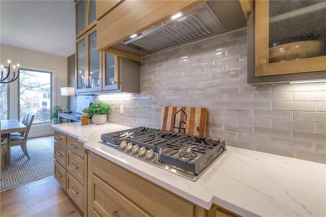 kitchen with custom exhaust hood, tasteful backsplash, light stone counters, light wood-type flooring, and stainless steel gas stovetop