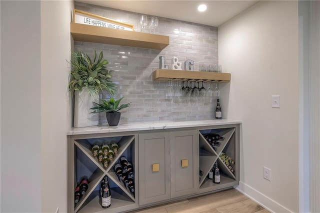 bar with gray cabinets, decorative backsplash, and light hardwood / wood-style flooring