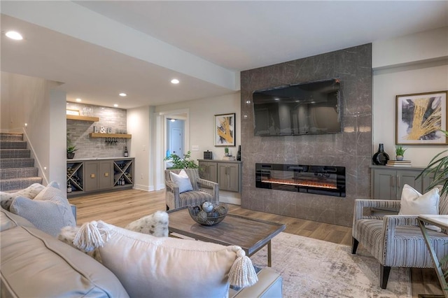 living room with a tiled fireplace, bar, and light wood-type flooring