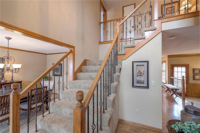 stairs with a chandelier, wood finished floors, a towering ceiling, and crown molding