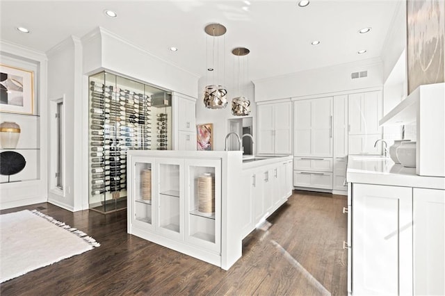 kitchen with dark wood-style flooring, a center island with sink, light countertops, visible vents, and glass insert cabinets