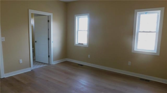 unfurnished room featuring baseboards, visible vents, and wood finished floors