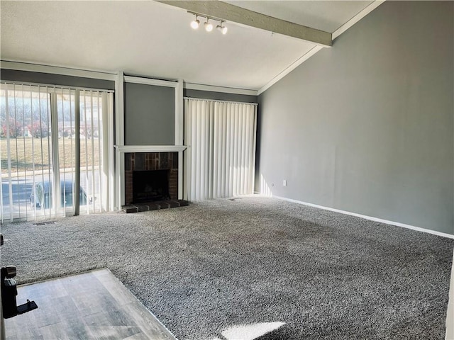 unfurnished living room with rail lighting, vaulted ceiling with beams, a brick fireplace, ornamental molding, and carpet