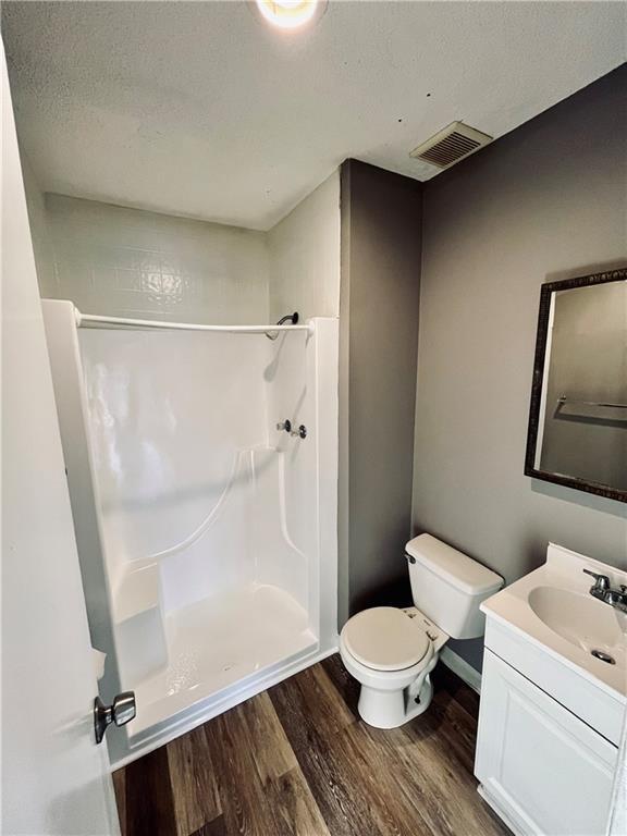 bathroom with walk in shower, toilet, a textured ceiling, vanity, and hardwood / wood-style flooring