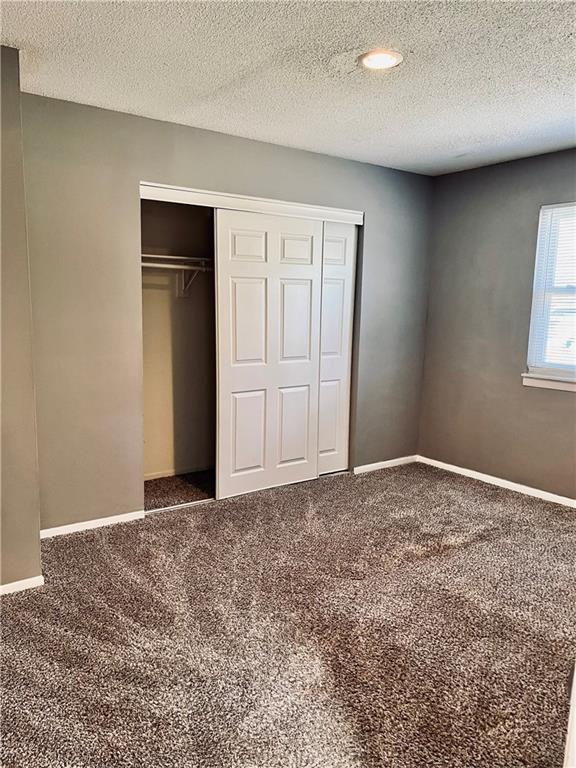 unfurnished bedroom featuring a textured ceiling, a closet, and dark colored carpet