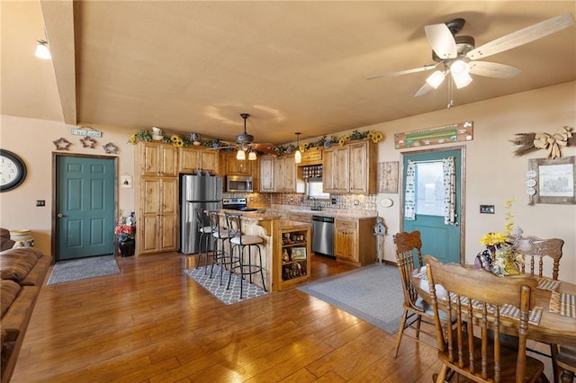 kitchen with appliances with stainless steel finishes, dark wood-type flooring, a breakfast bar area, and tasteful backsplash