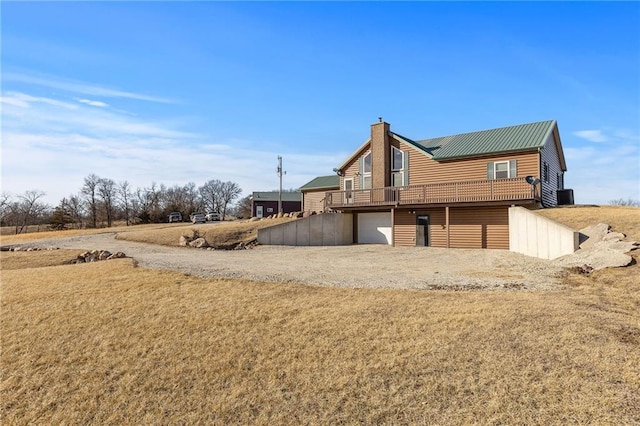 back of property featuring a deck, metal roof, driveway, a chimney, and log veneer siding