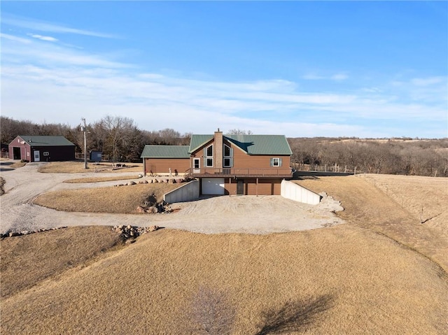 view of front of home featuring a garage, dirt driveway, a chimney, and metal roof