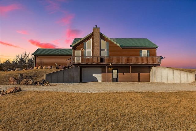 rear view of house with a chimney, an attached garage, metal roof, log veneer siding, and driveway