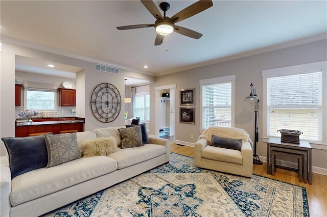 living area with crown molding, light wood-type flooring, visible vents, and baseboards