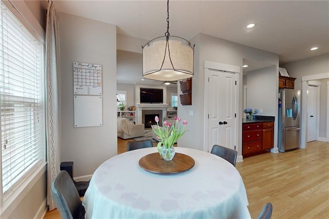 dining room featuring light wood-style floors, recessed lighting, a lit fireplace, and baseboards