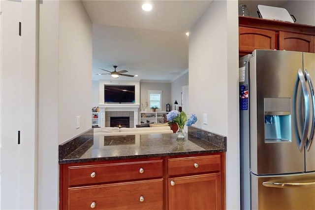 kitchen featuring ceiling fan, a tile fireplace, open floor plan, dark stone counters, and stainless steel fridge