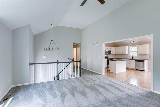 unfurnished living room with high vaulted ceiling, sink, light colored carpet, and ceiling fan