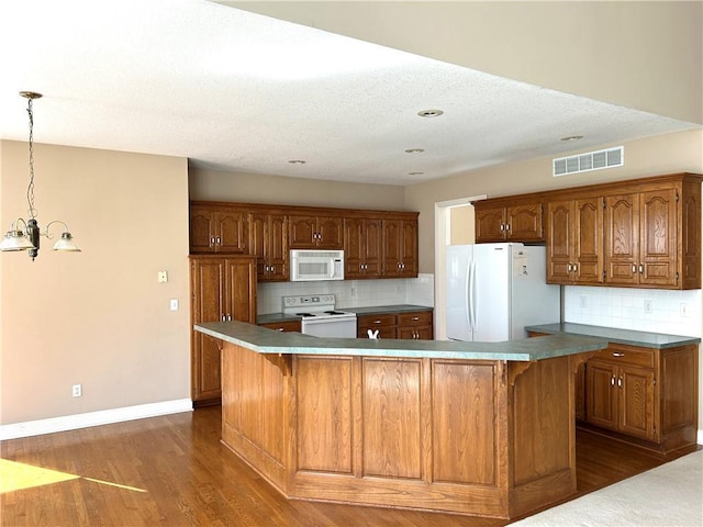 kitchen with visible vents, brown cabinets, dark wood-style floors, white appliances, and baseboards