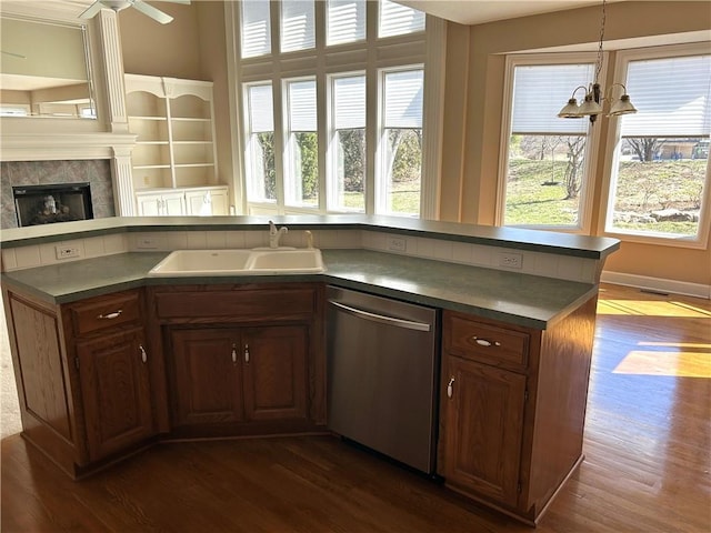 kitchen with stainless steel dishwasher, dark countertops, a fireplace, and a sink