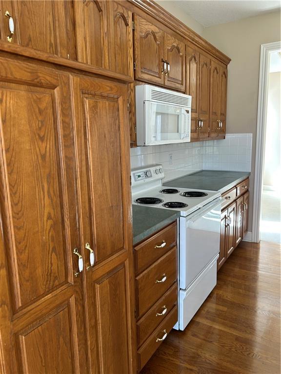 kitchen with dark wood-style floors, decorative backsplash, brown cabinets, and white appliances