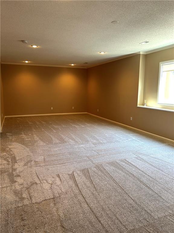 carpeted spare room featuring baseboards, a textured ceiling, and crown molding